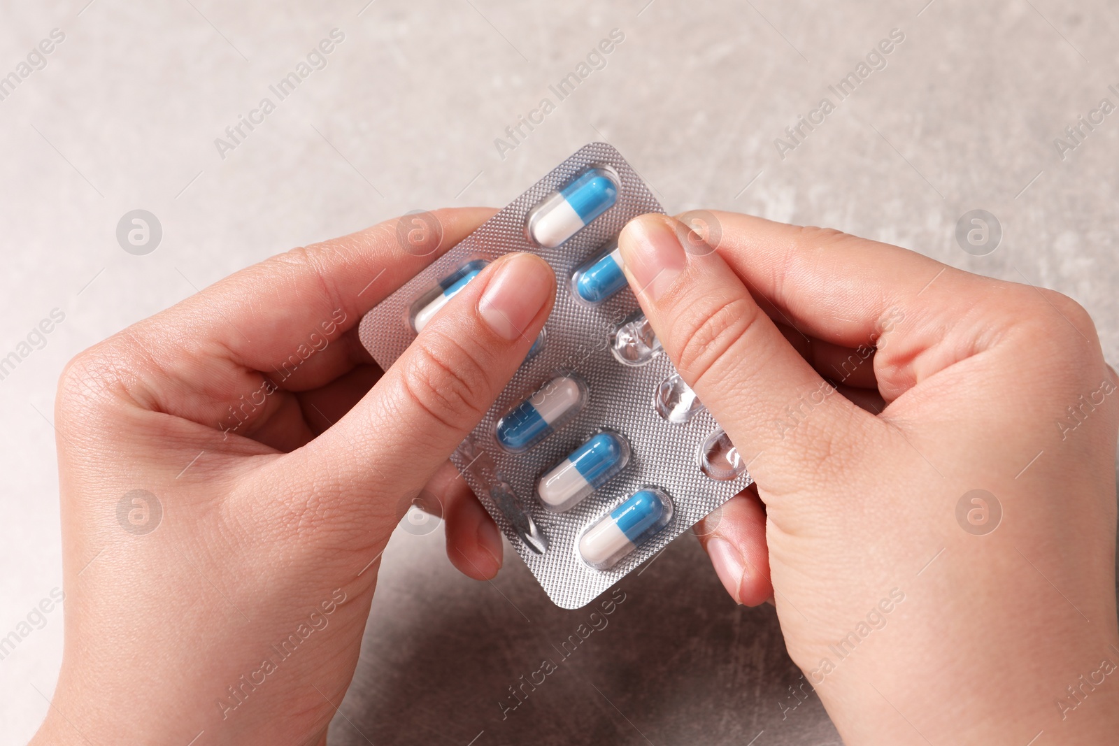 Photo of Woman taking pill out from blister pack at grey table, closeup