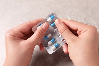 Photo of Woman taking pill out from blister pack at grey table, closeup
