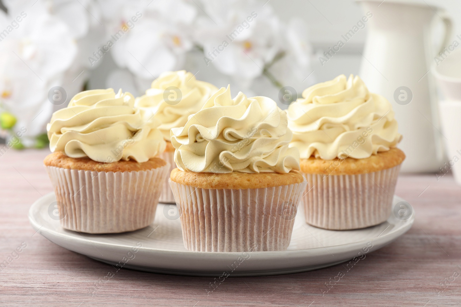 Photo of Tasty cupcakes with vanilla cream on pink wooden table, closeup