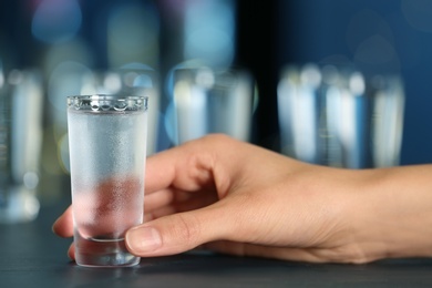 Woman with shot of vodka at table in bar, closeup