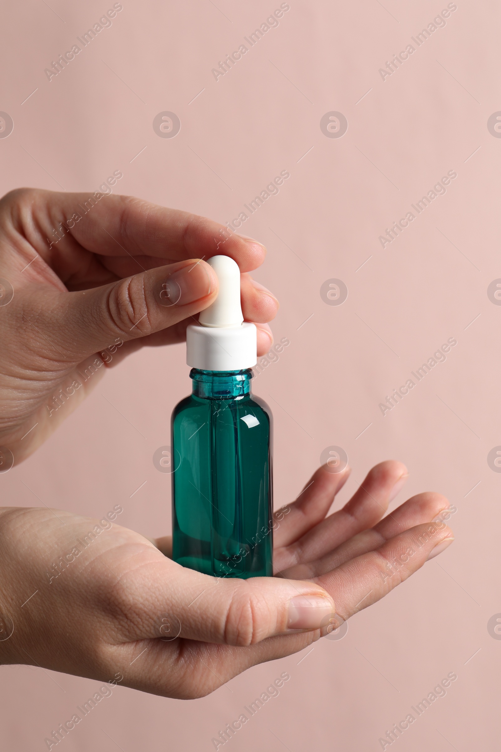 Photo of Woman with bottle of cosmetic serum on light pink background, closeup