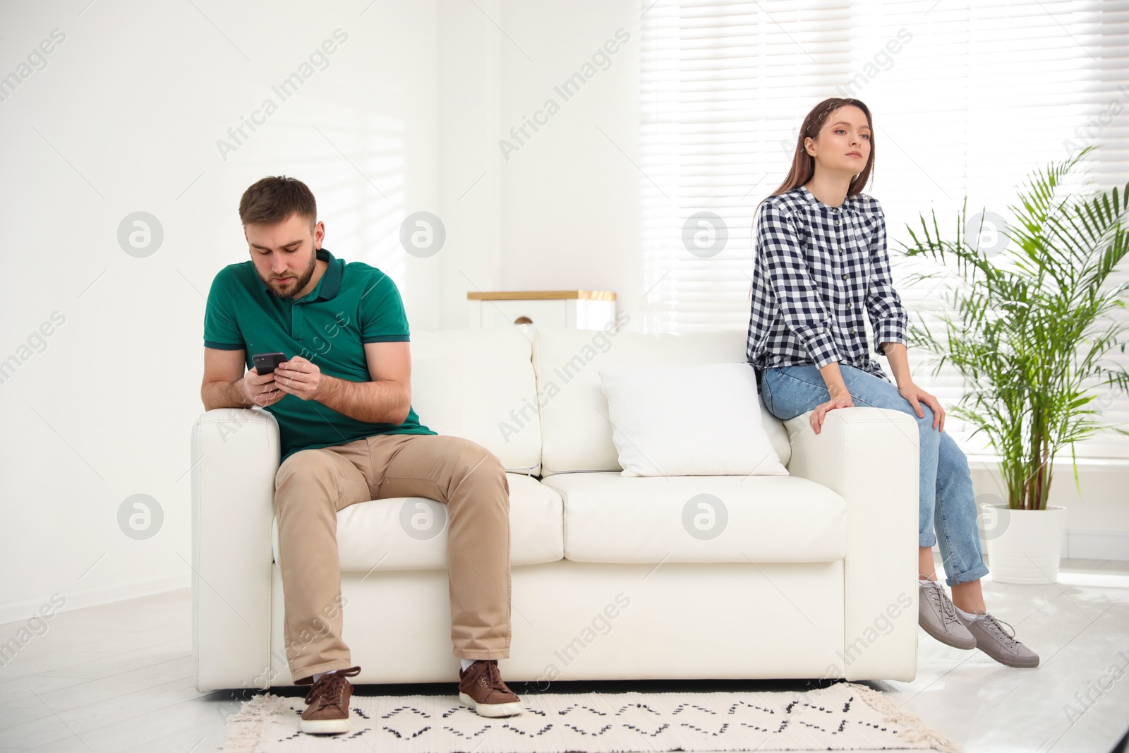 Photo of Young man preferring smartphone over his girlfriend at home. Relationship problems