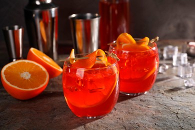 Aperol spritz cocktail, ice cubes and orange slices in glasses on grey textured table