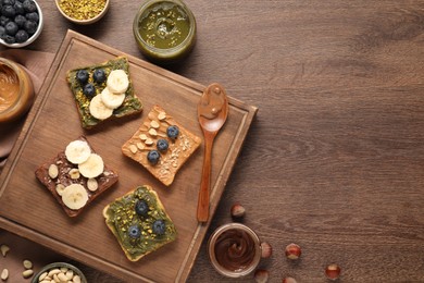 Photo of Toasts with different nut butters, blueberries, banana and nuts on wooden table, flat lay. Space for text