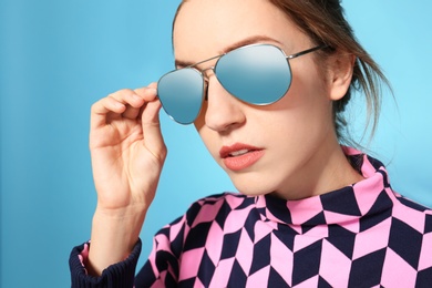 Young woman wearing stylish sunglasses on blue background