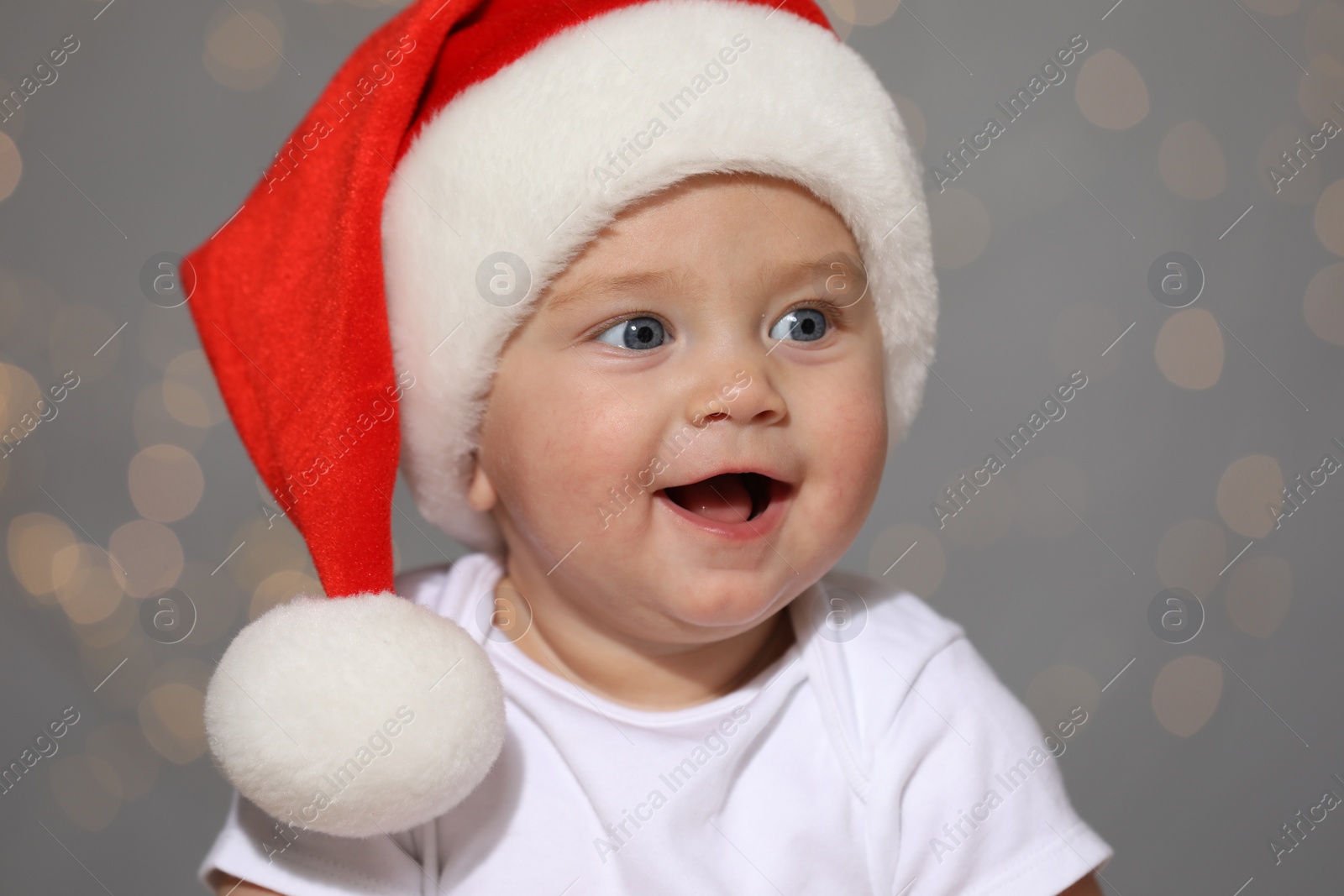 Photo of Cute baby in Santa hat against blurred lights. Christmas celebration