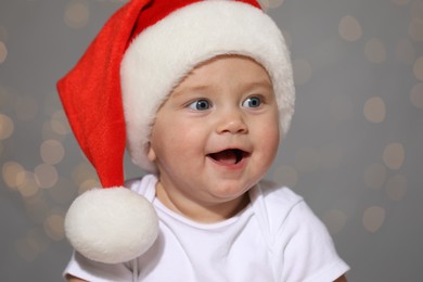 Cute baby in Santa hat against blurred lights. Christmas celebration