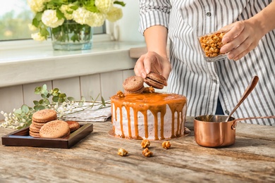 Photo of Young woman decorating delicious caramel cake at table