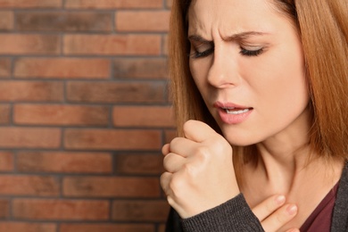 Woman suffering from cough near brick wall. Space for text