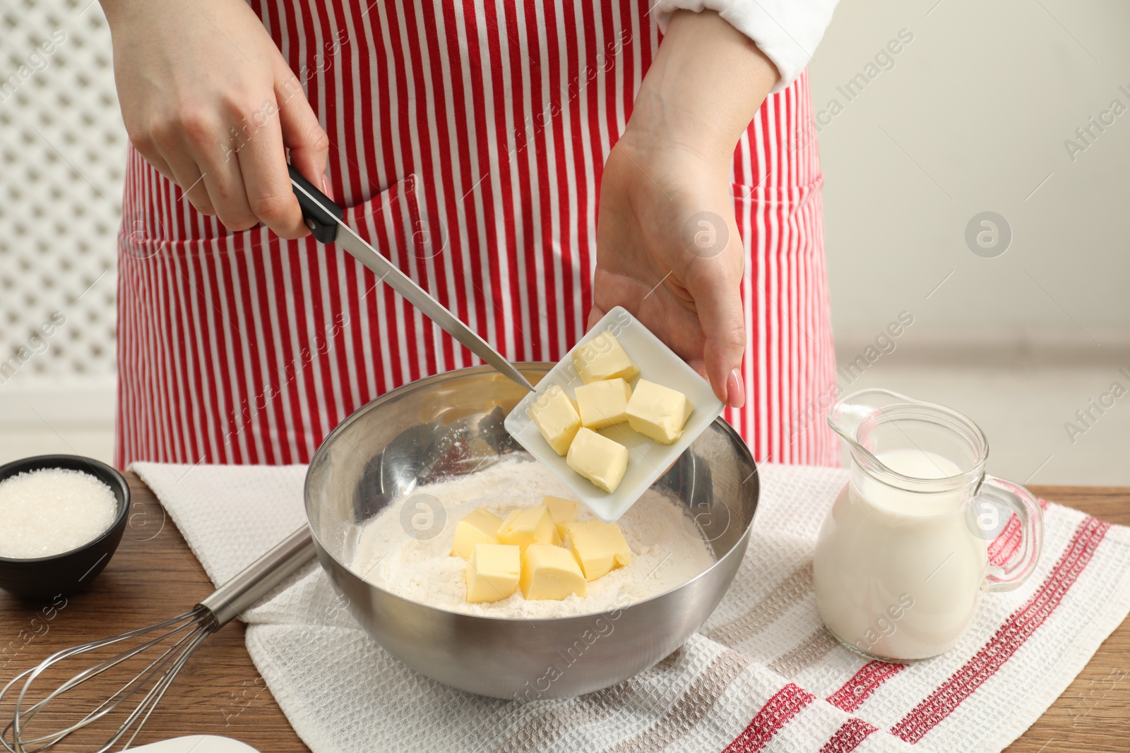 Photo of Woman adding fresh butter into bowl with flour at wooden table, closeup