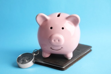 Photo of Piggy bank with passport and compass on color background. Travel agency