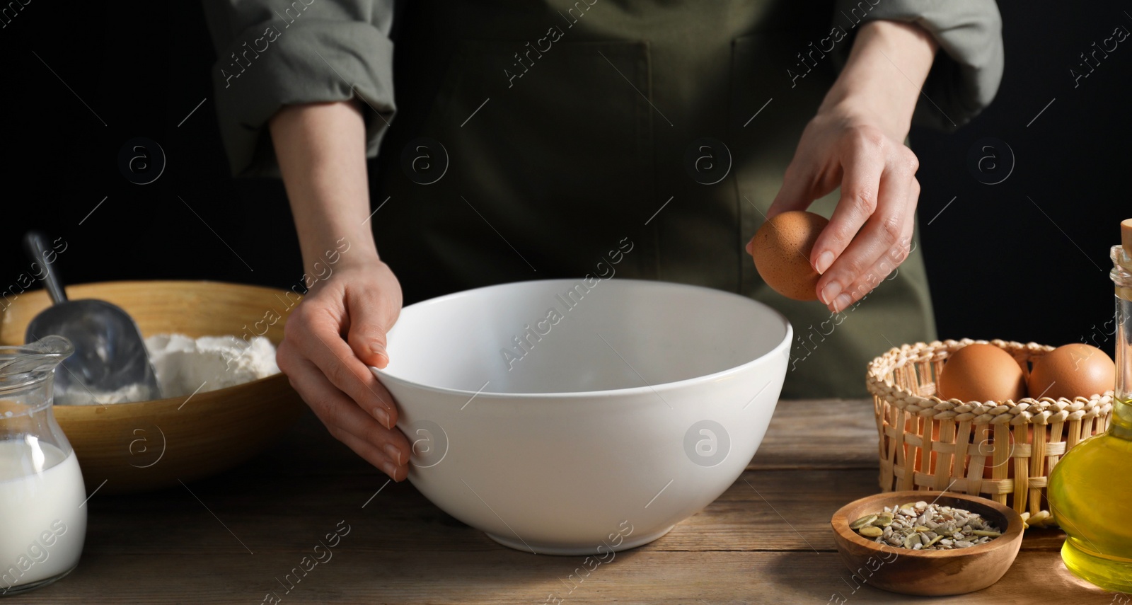 Photo of Making bread. Woman adding egg into dough at wooden table on dark background, closeup