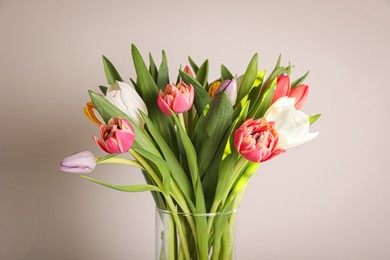 Photo of Beautiful bouquet of colorful tulips in glass vase on beige background