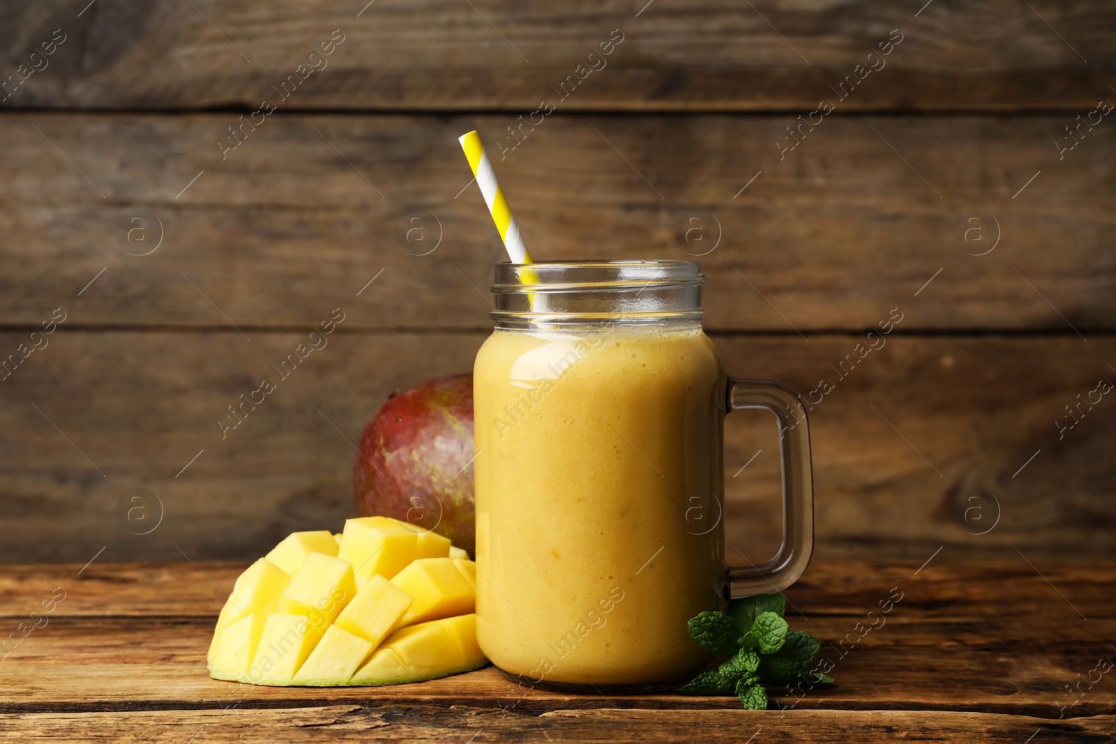 Photo of Mason jar with delicious fruit smoothie and fresh mango on wooden table