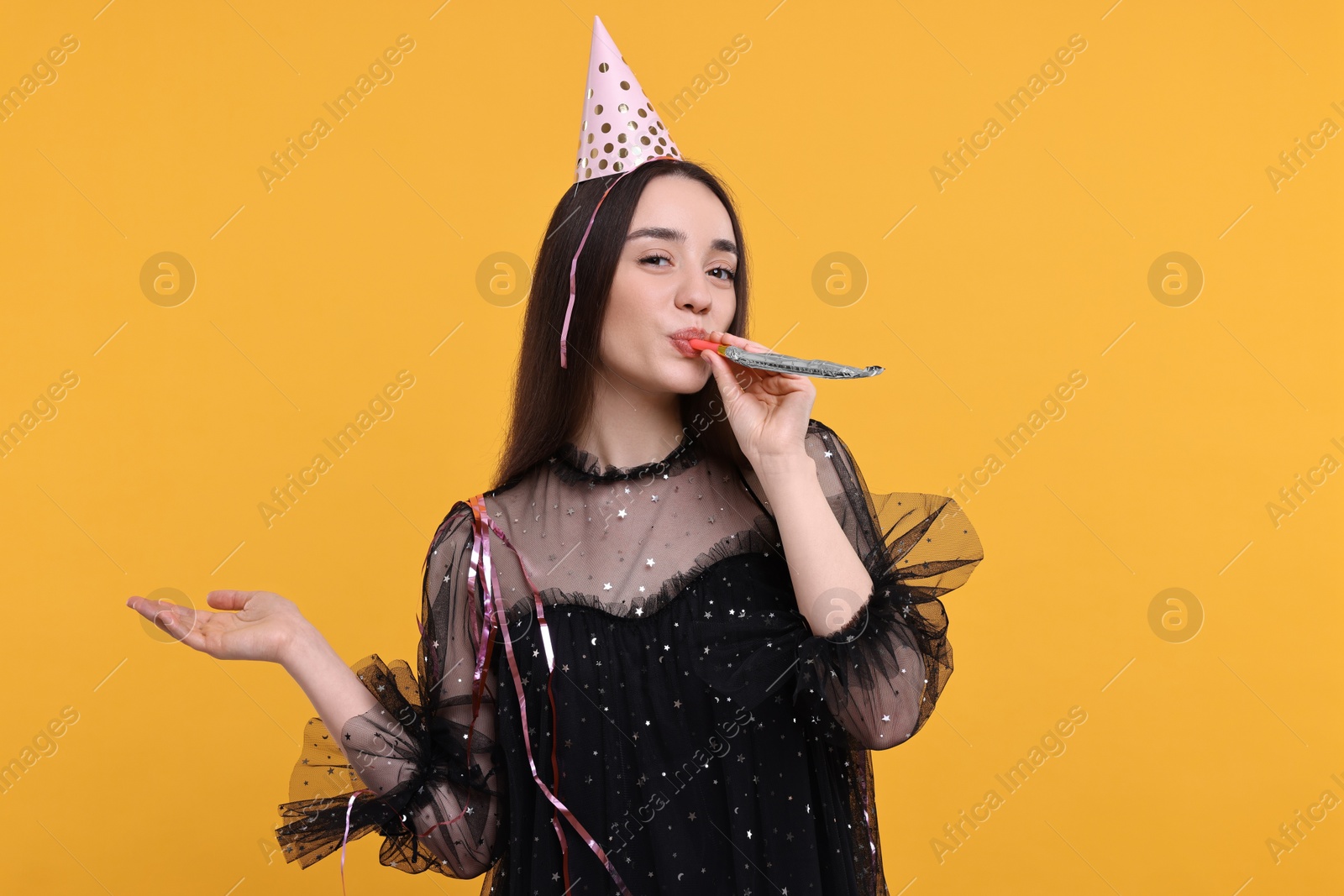 Photo of Woman in party hat with blower and streamers on orange background