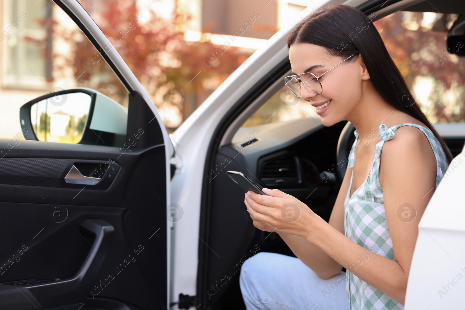 Photo of Happy young woman with smartphone sitting in car