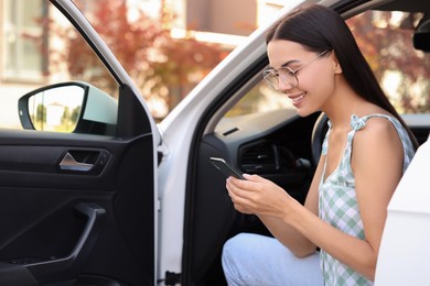 Happy young woman with smartphone sitting in car