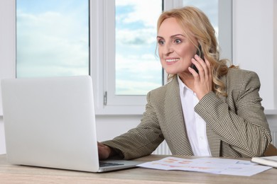 Photo of Lady boss talking on smartphone near laptop in office. Successful businesswoman