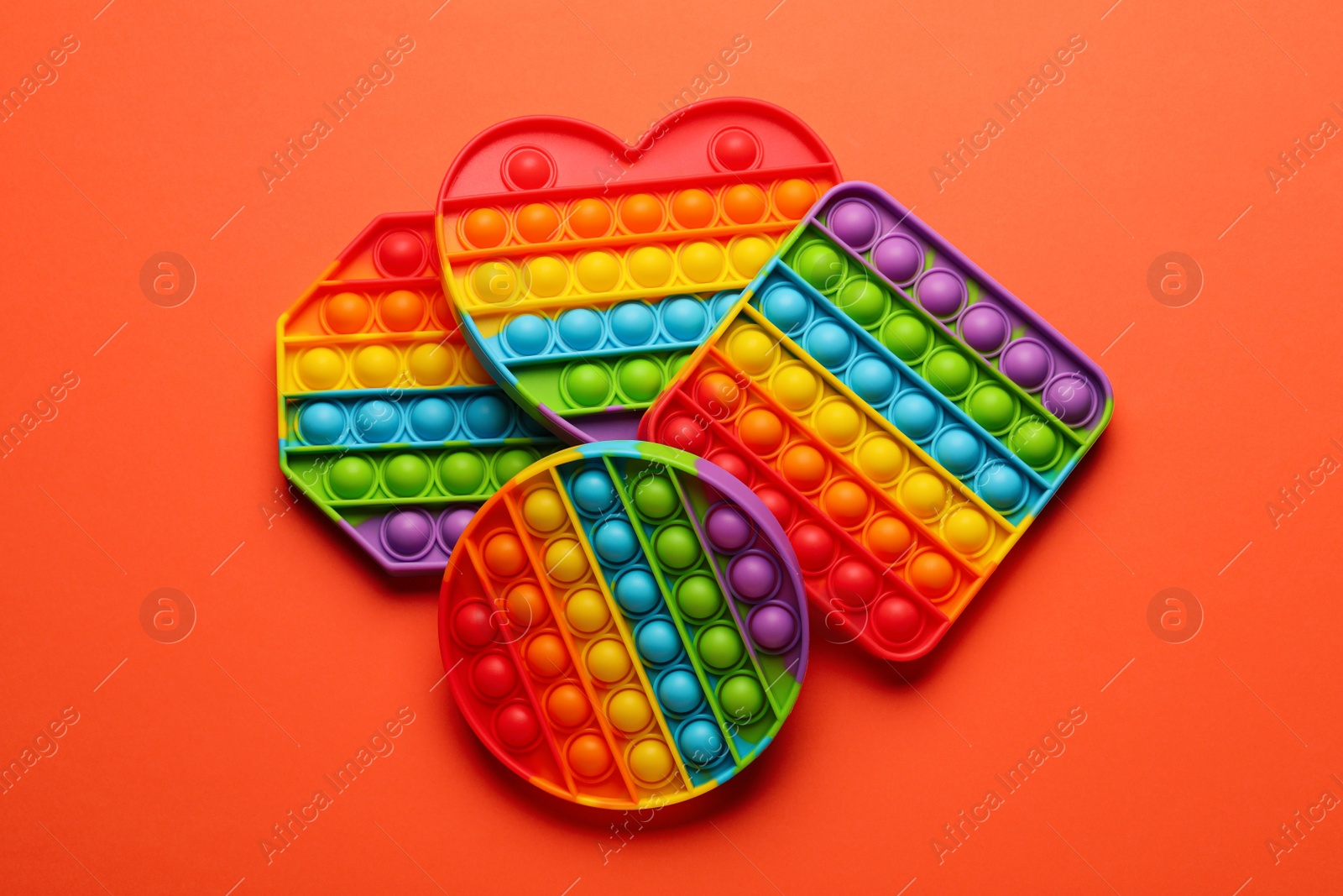 Photo of Rainbow pop it fidget toys on coral background, flat lay
