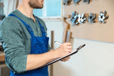 Photo of Young working man in uniform making notes at carpentry shop