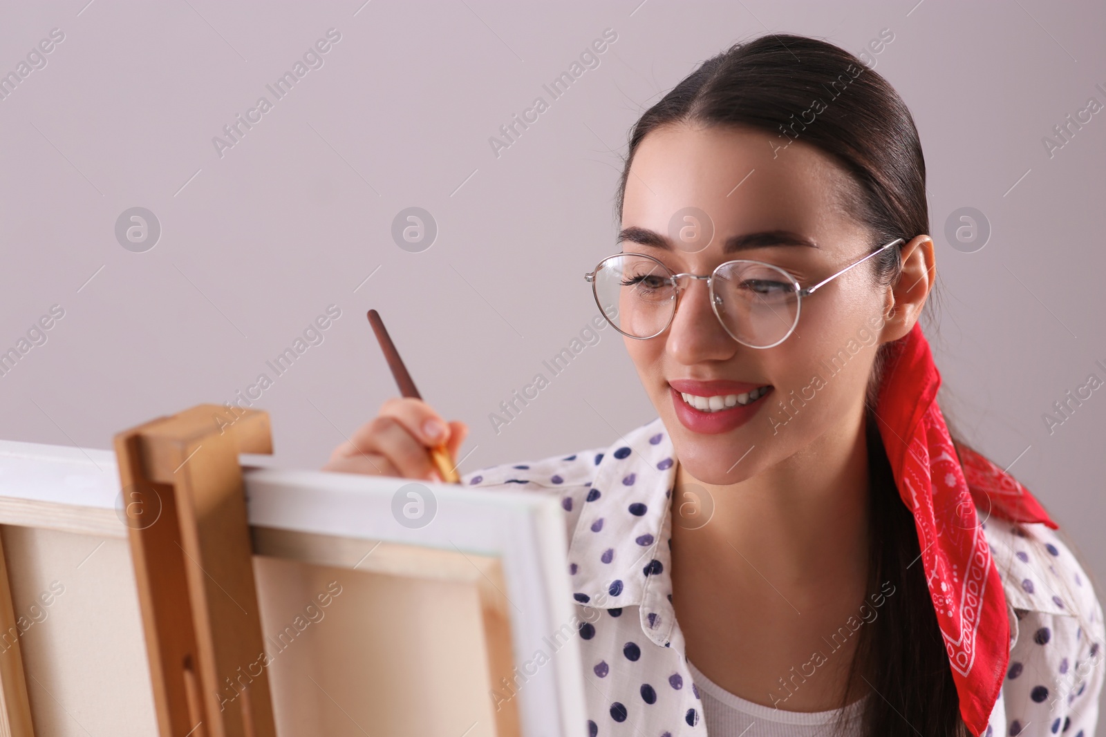 Photo of Happy woman artist drawing picture on canvas against grey background