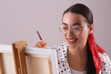 Photo of Happy woman artist drawing picture on canvas against grey background
