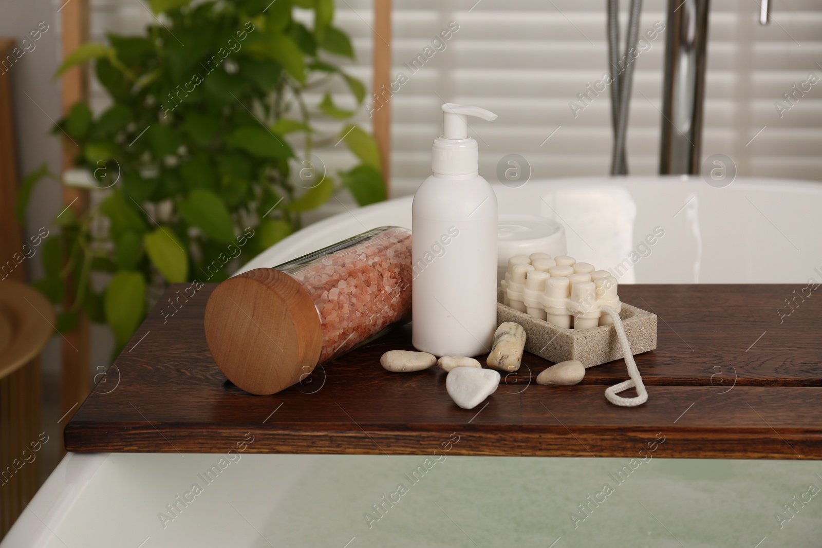 Photo of Wooden board with spa products on bath tub in bathroom