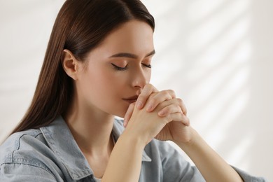 Photo of Religious young woman with clasped hands praying indoors, closeup