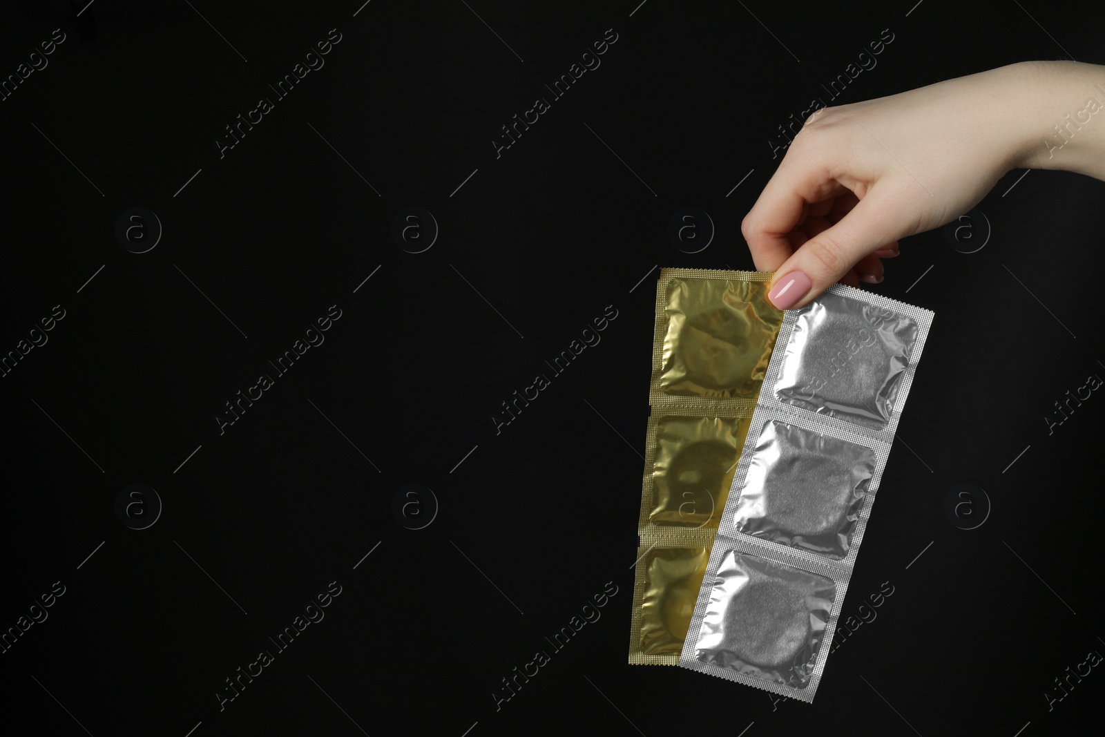 Photo of Woman holding condoms on black background, closeup. Space for text