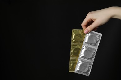 Woman holding condoms on black background, closeup. Space for text