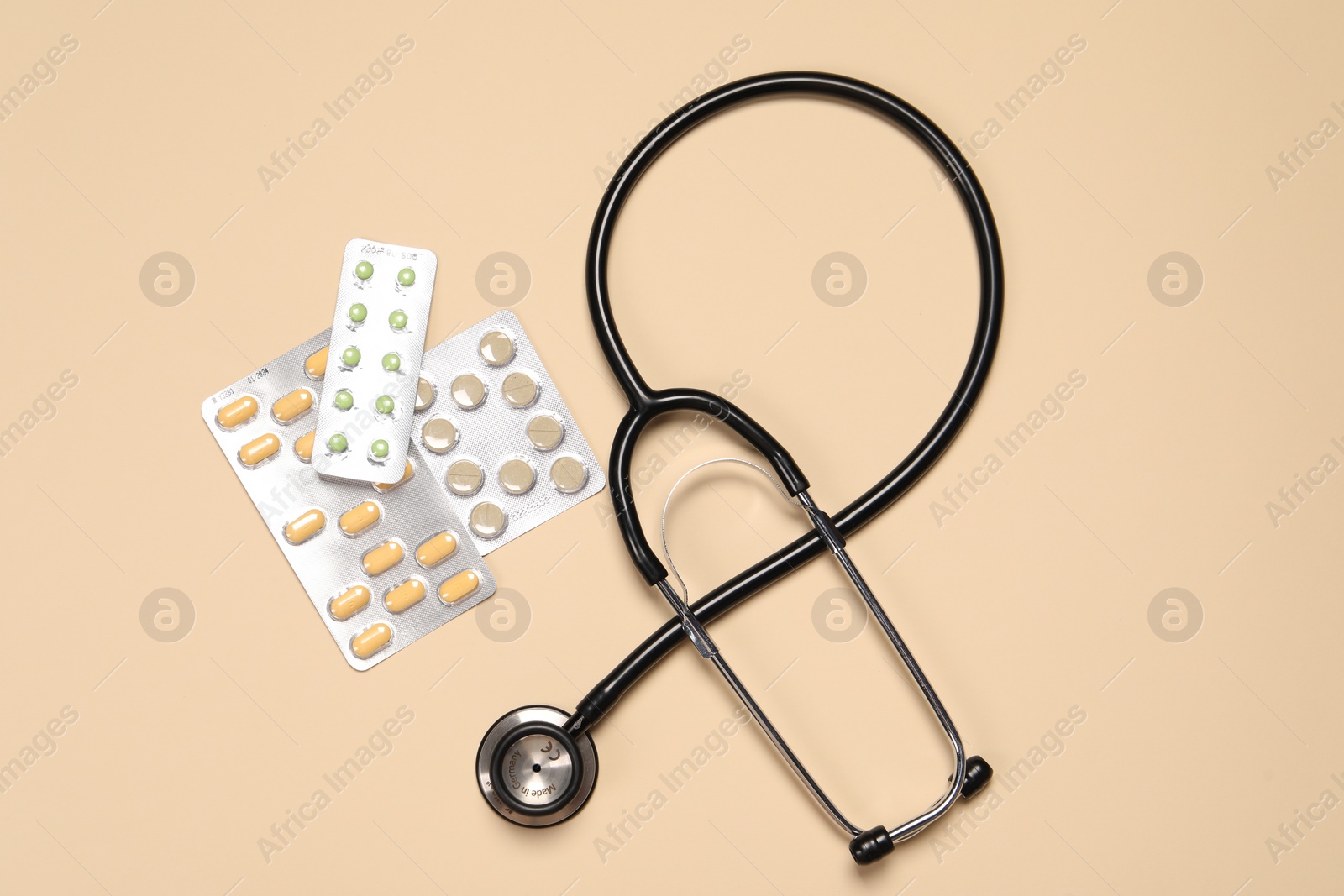 Photo of Stethoscope and pills on beige background, flat lay. Medical tool