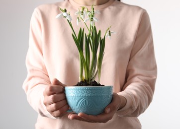 Woman holding turquoise cup with planted snowdrops on light background, closeup