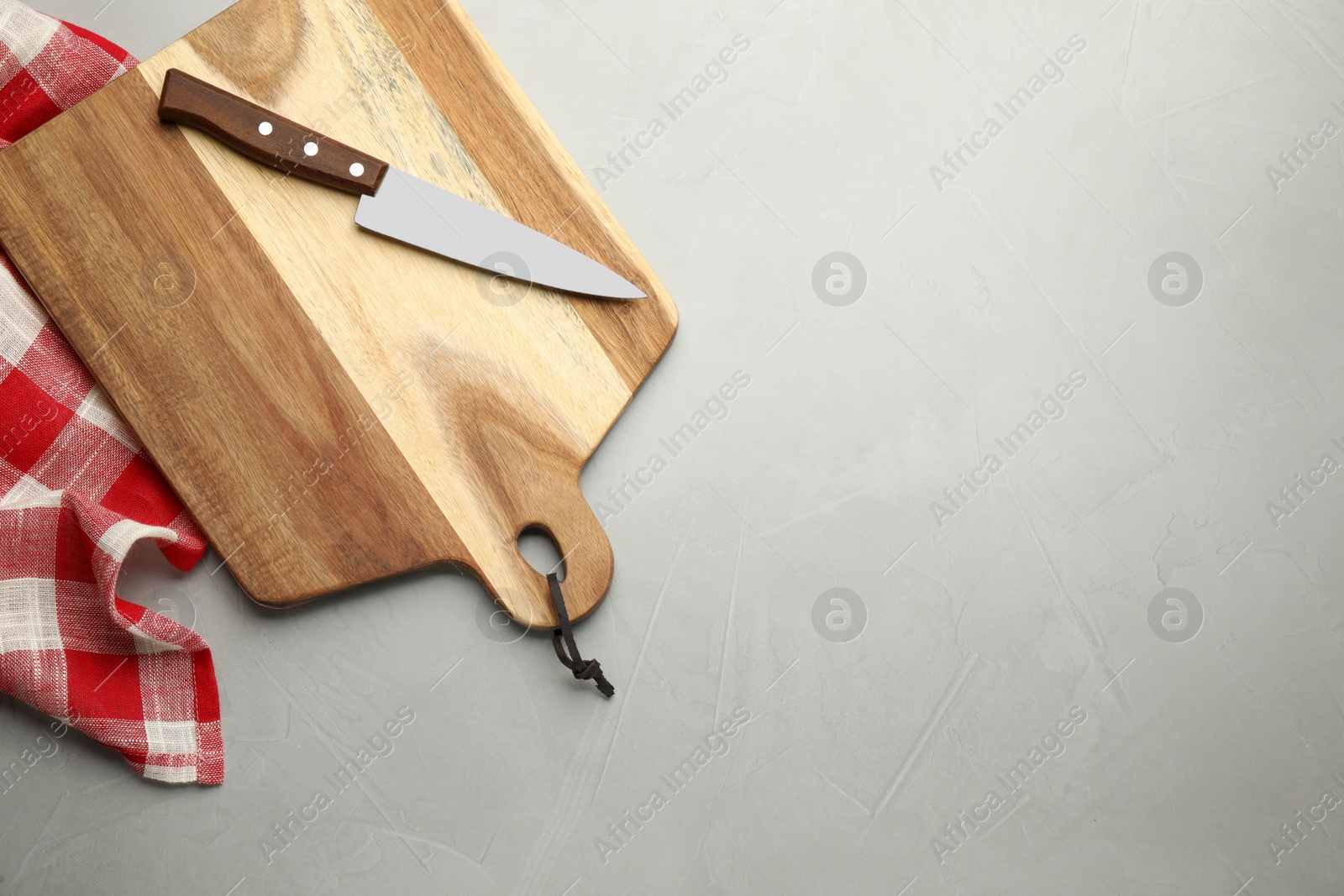 Photo of Wooden cutting board, knife and kitchen towel on light grey table, flat lay. Cooking utensils