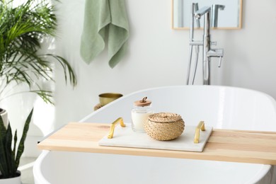 Photo of Tray with wicker box and candle on tub in bathroom. Interior design