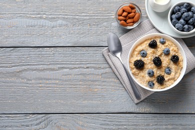 Photo of Tasty oatmeal porridge with blackberries and blueberries served on light grey wooden table, flat lay. Space for text