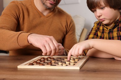 Photo of Father playing checkers with his son at table in room, closeup