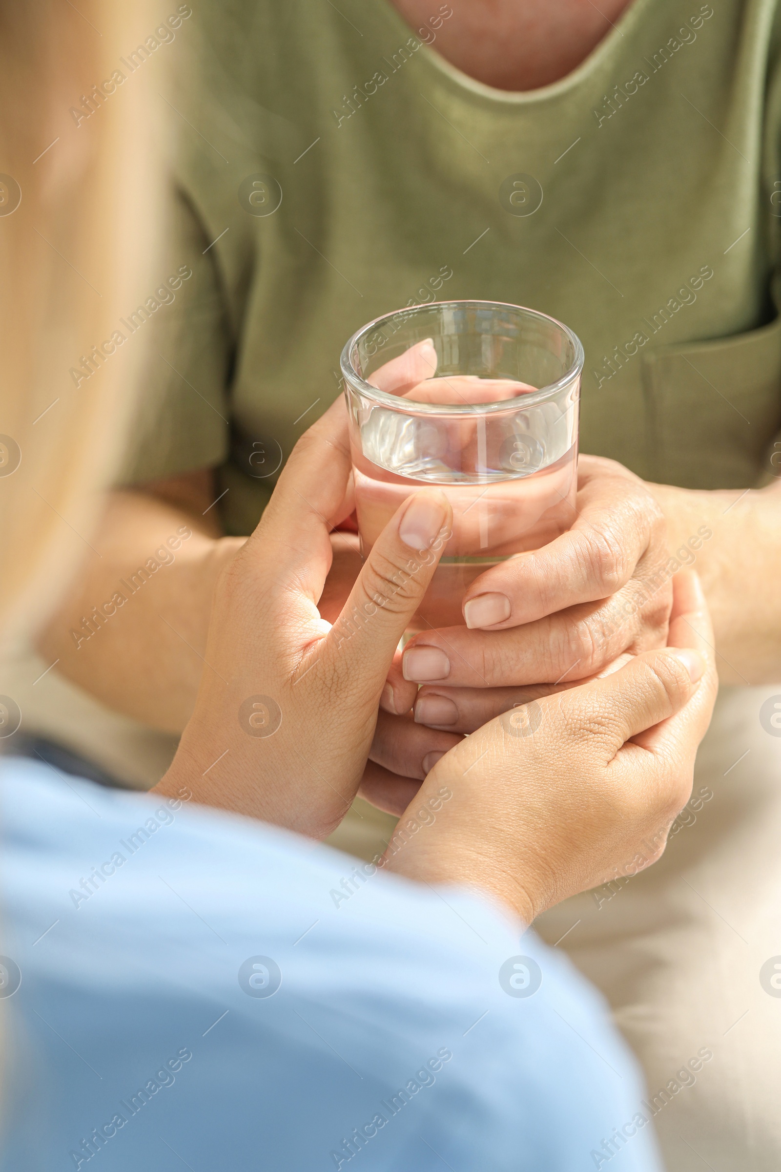 Photo of Caretaker giving glass of water to elderly woman, closeup