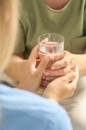 Photo of Caretaker giving glass of water to elderly woman, closeup