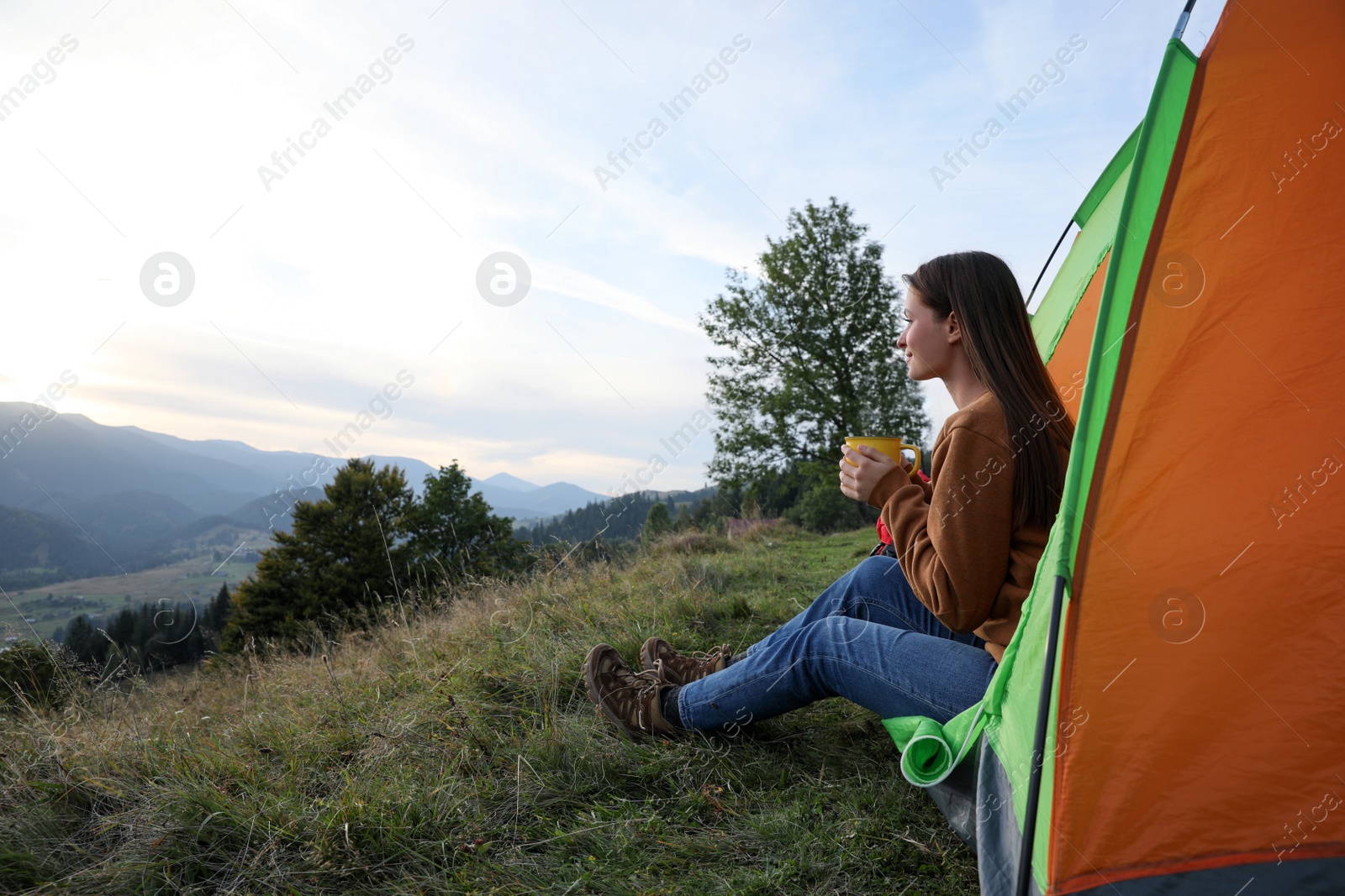 Photo of Young woman with cup of drink in camping tent on mountain slope, space for text