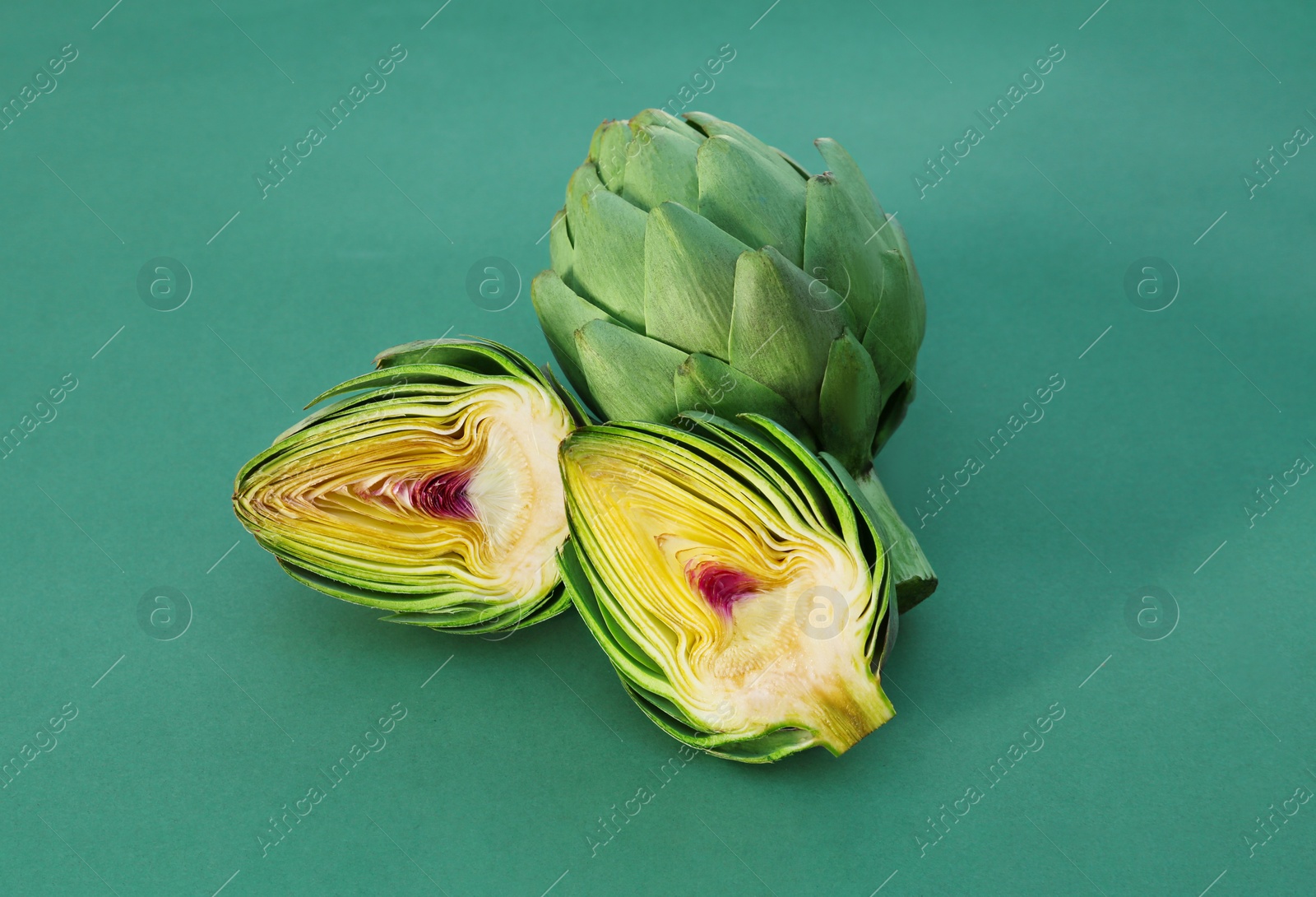Photo of Cut and whole fresh raw artichokes on green background