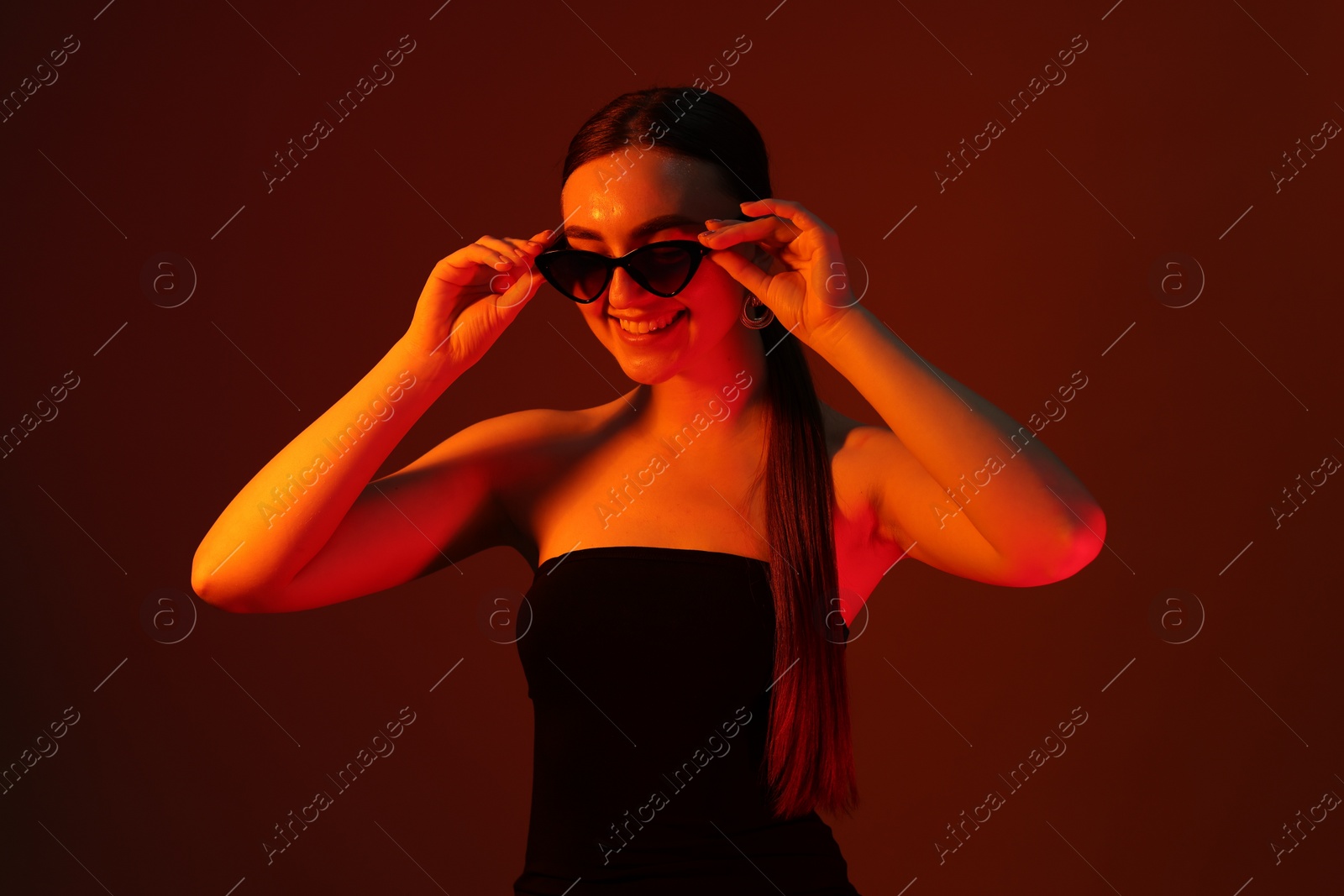 Photo of Portrait of beautiful young woman in sunglasses on color background with neon lights