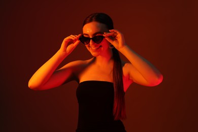 Photo of Portrait of beautiful young woman in sunglasses on color background with neon lights