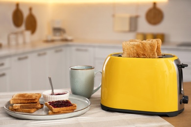 Modern toaster and tasty breakfast on wooden table in kitchen