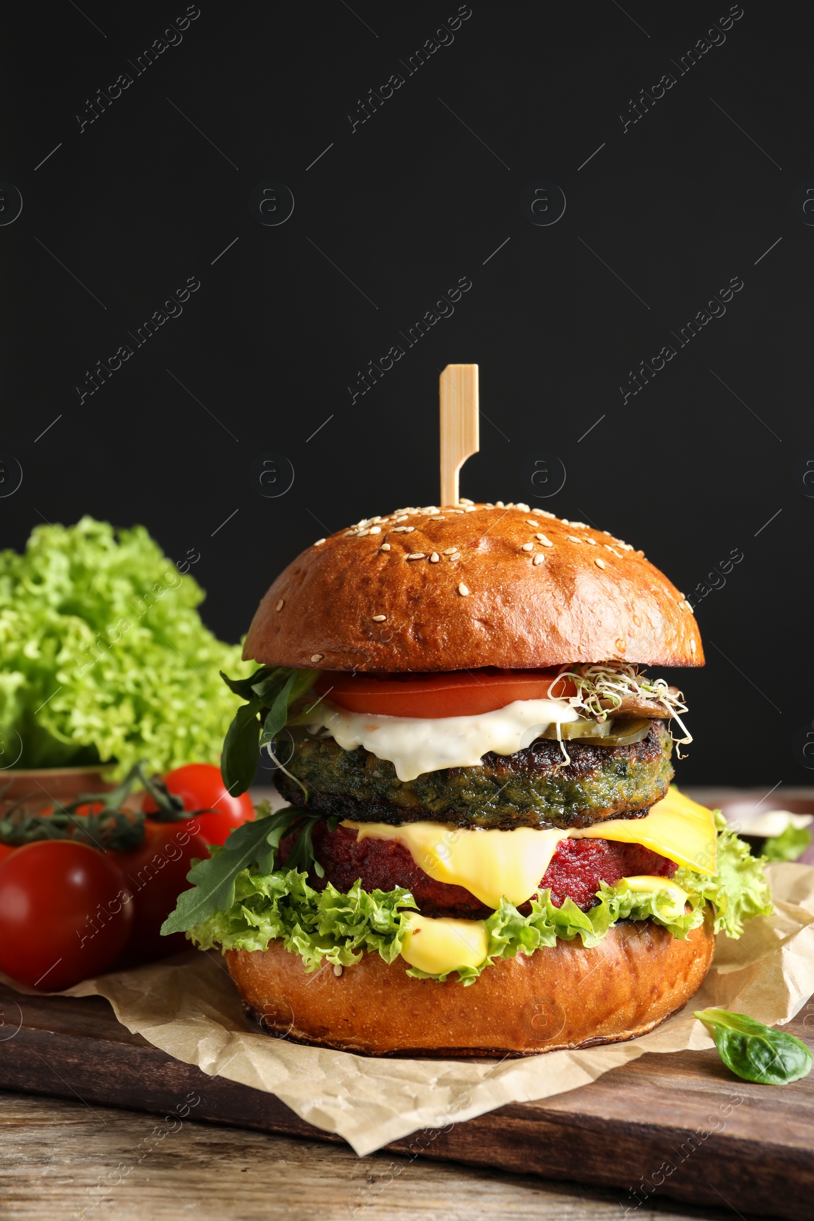 Photo of Vegan burger and vegetables on table against dark background. Space for text