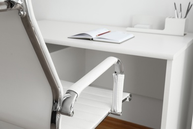 Modern office chair near table indoors, closeup. Stylish workplace interior