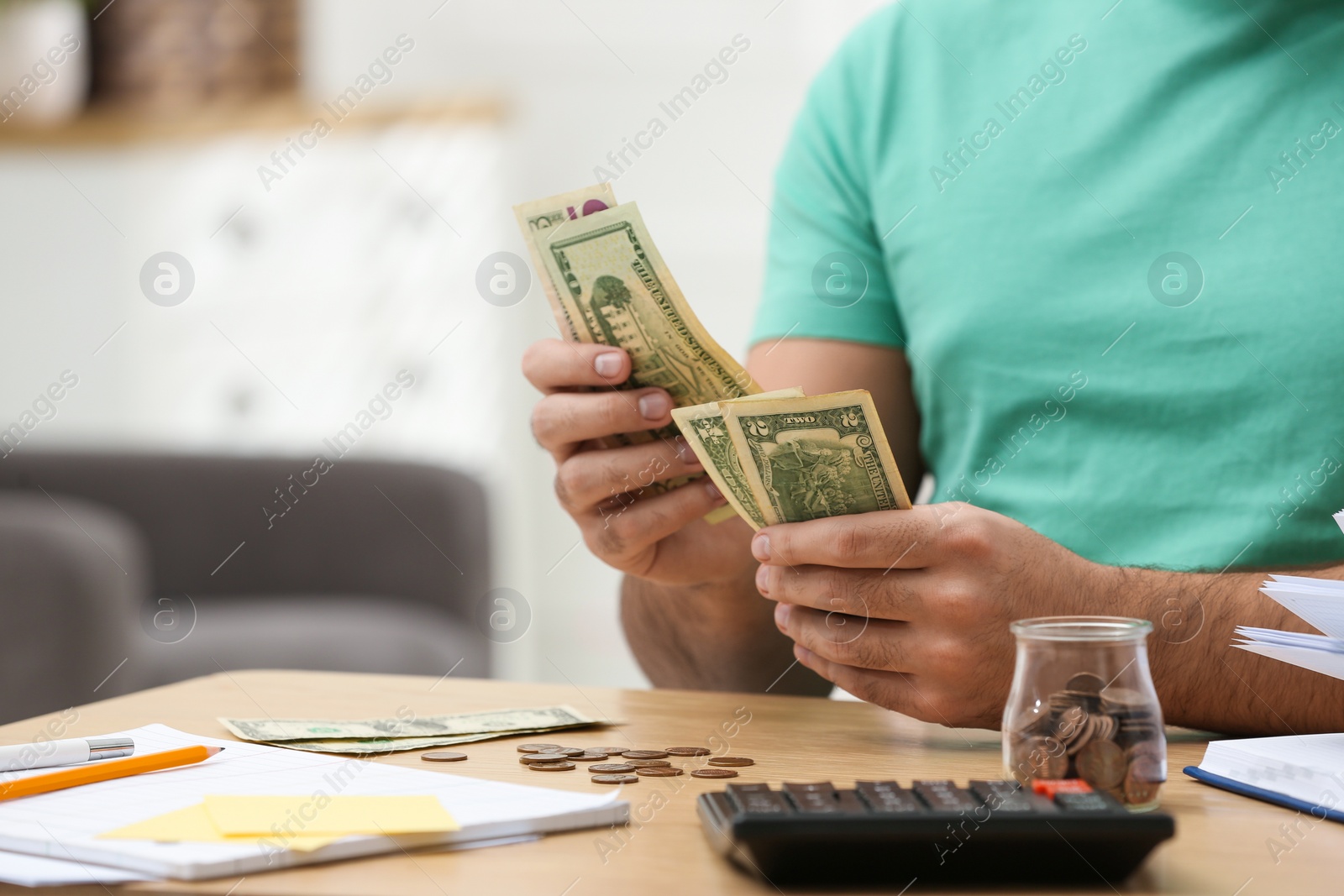 Photo of Young man counting money at wooden table indoors, closeup