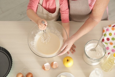 Photo of Little girl and her grandmother cooking at table with products, top view