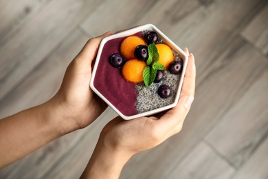 Woman holding bowl of tasty acai smoothie over wooden floor