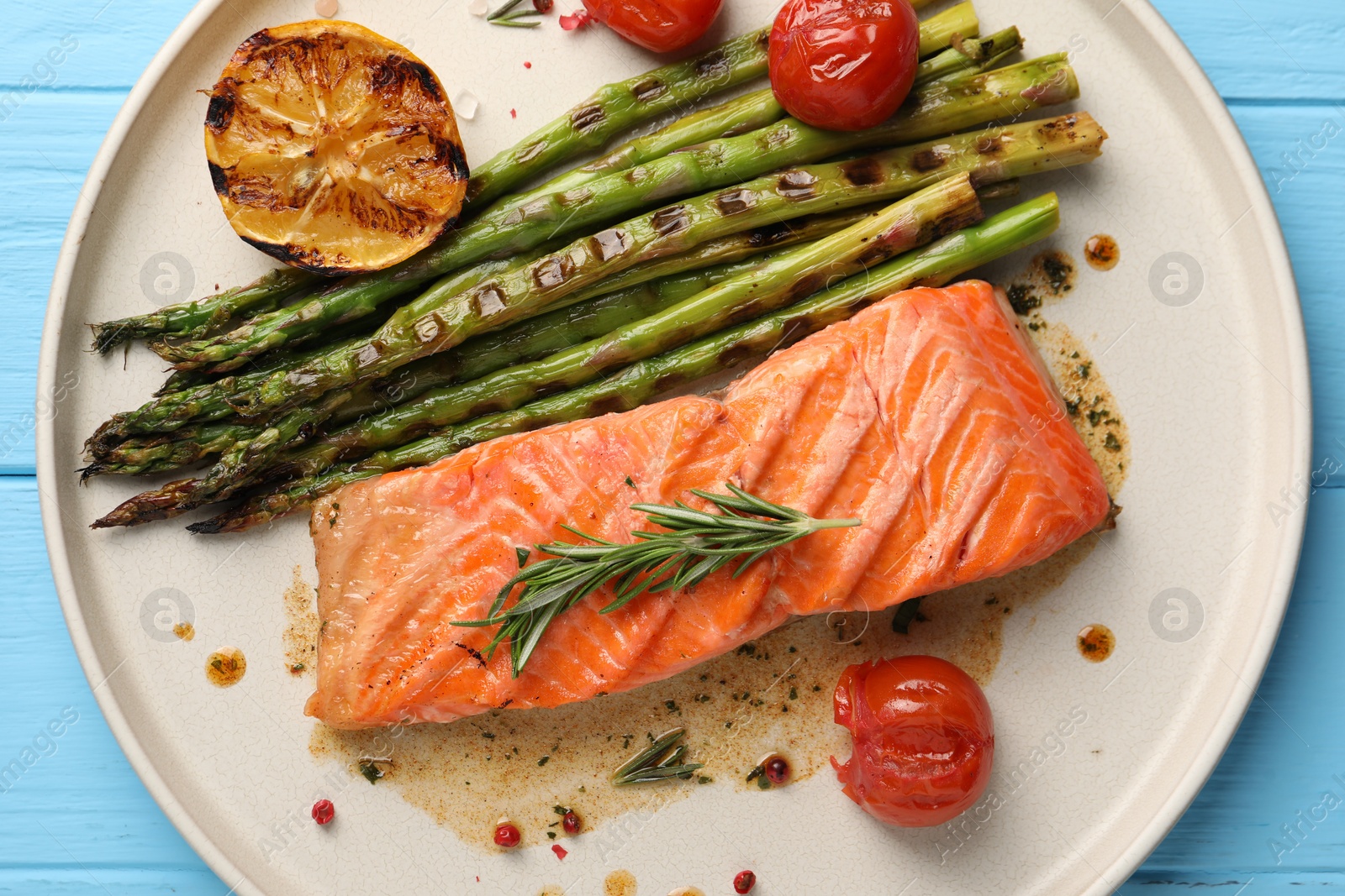 Photo of Tasty grilled salmon with tomatoes, asparagus and spices on light blue table, top view