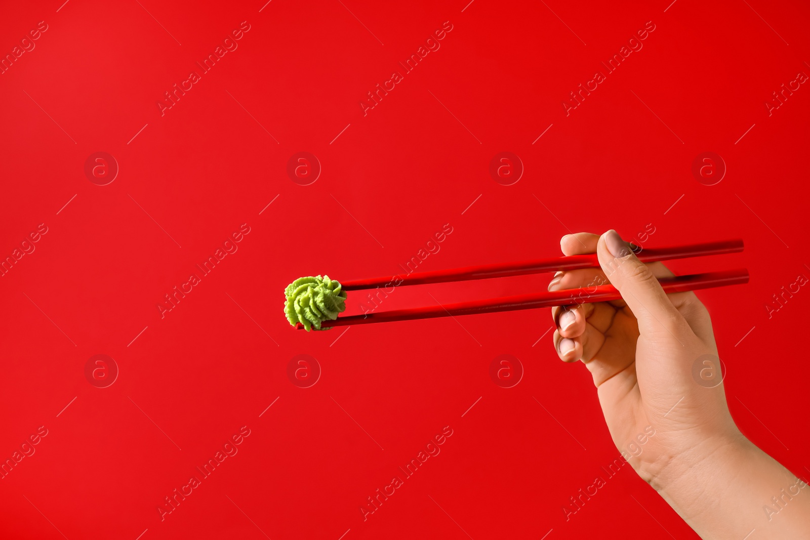 Photo of Woman holding swirl of wasabi paste with chopsticks on red background, closeup